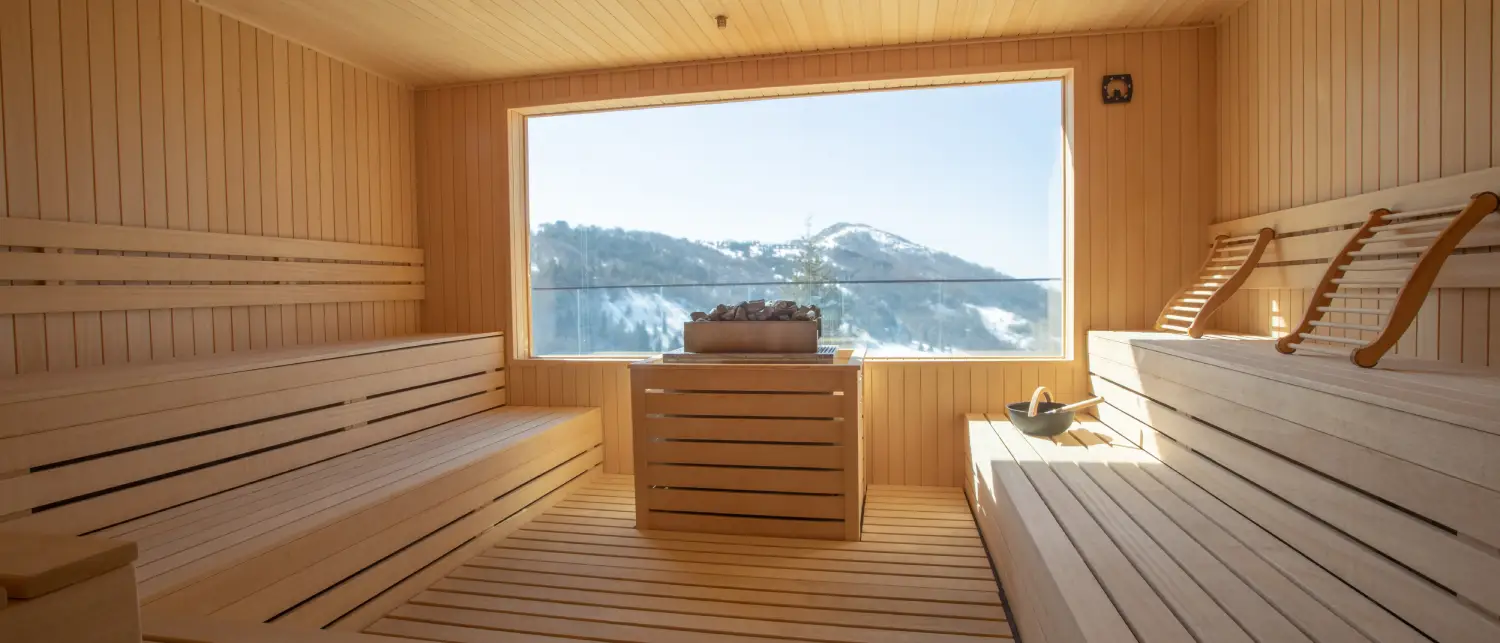 A finely detailed cedar sauna with a large window looks over snowy mountains